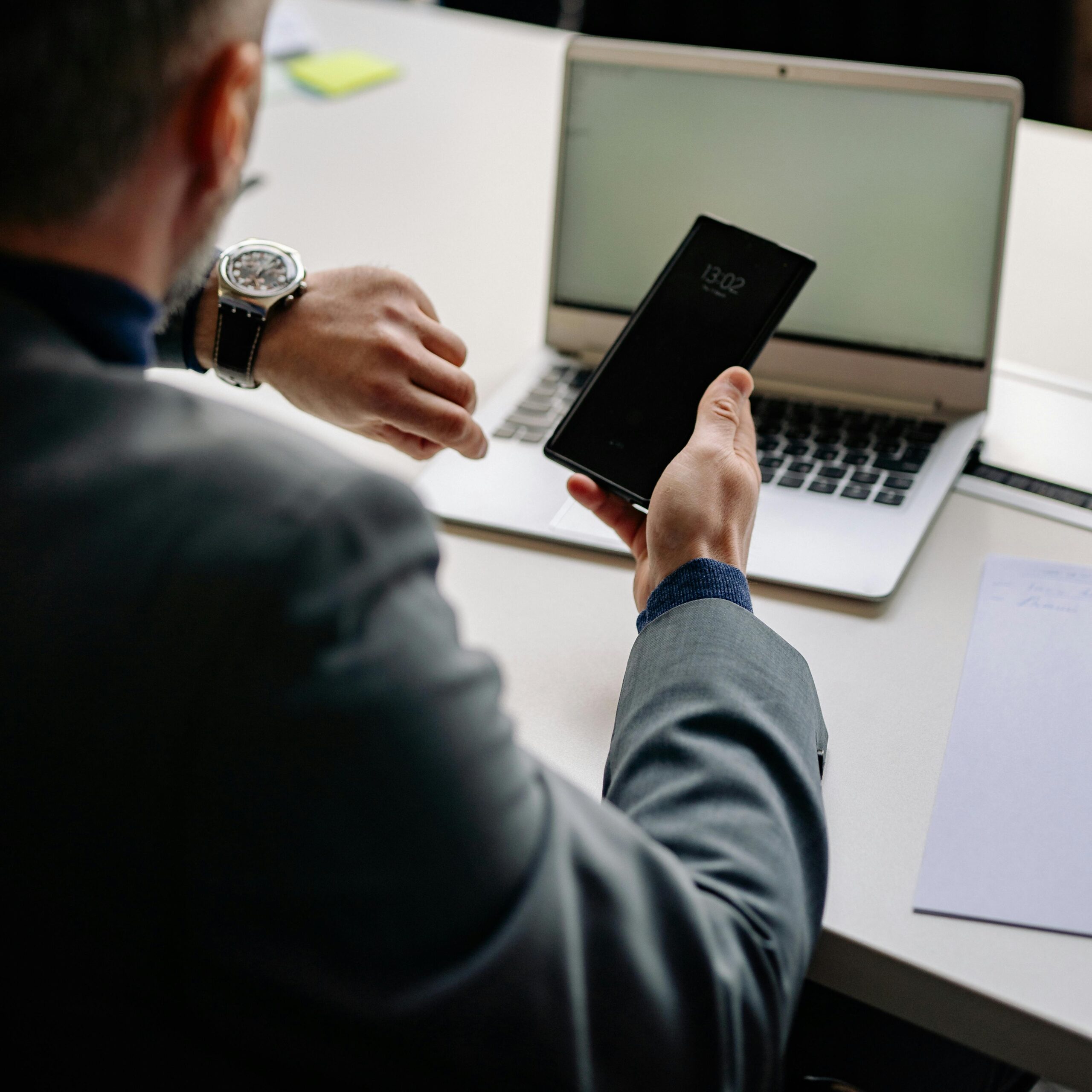 Man in office using smartphone and laptop, showing time management.